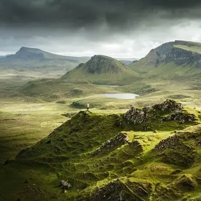 person standing in the middle of vast green mountain ranges