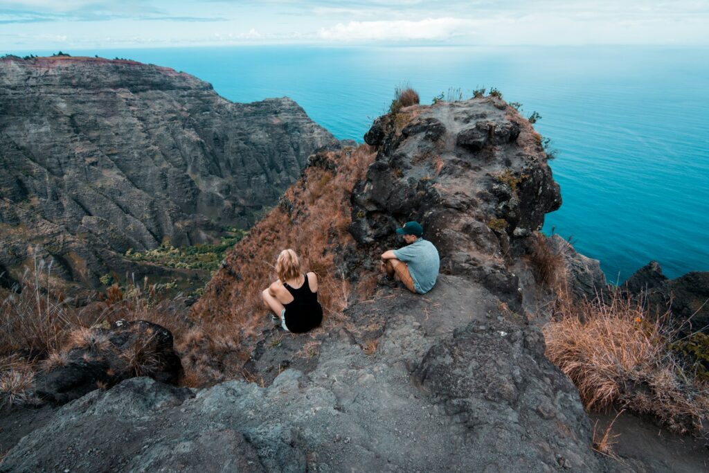 man and woman sitting on top of a mountain surrounded by ocean