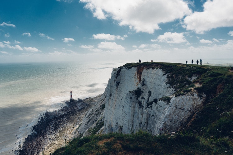 group of people standing on top of mountain above view of a lighthouse