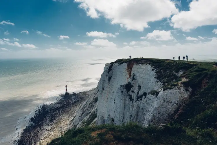 group of people standing on top of mountain above view of a lighthouse