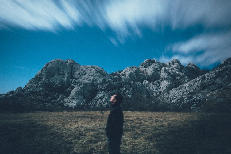 man standing in front of mountain looking up at sky