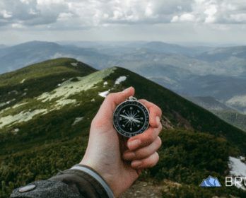 person holding compass with mountains in background